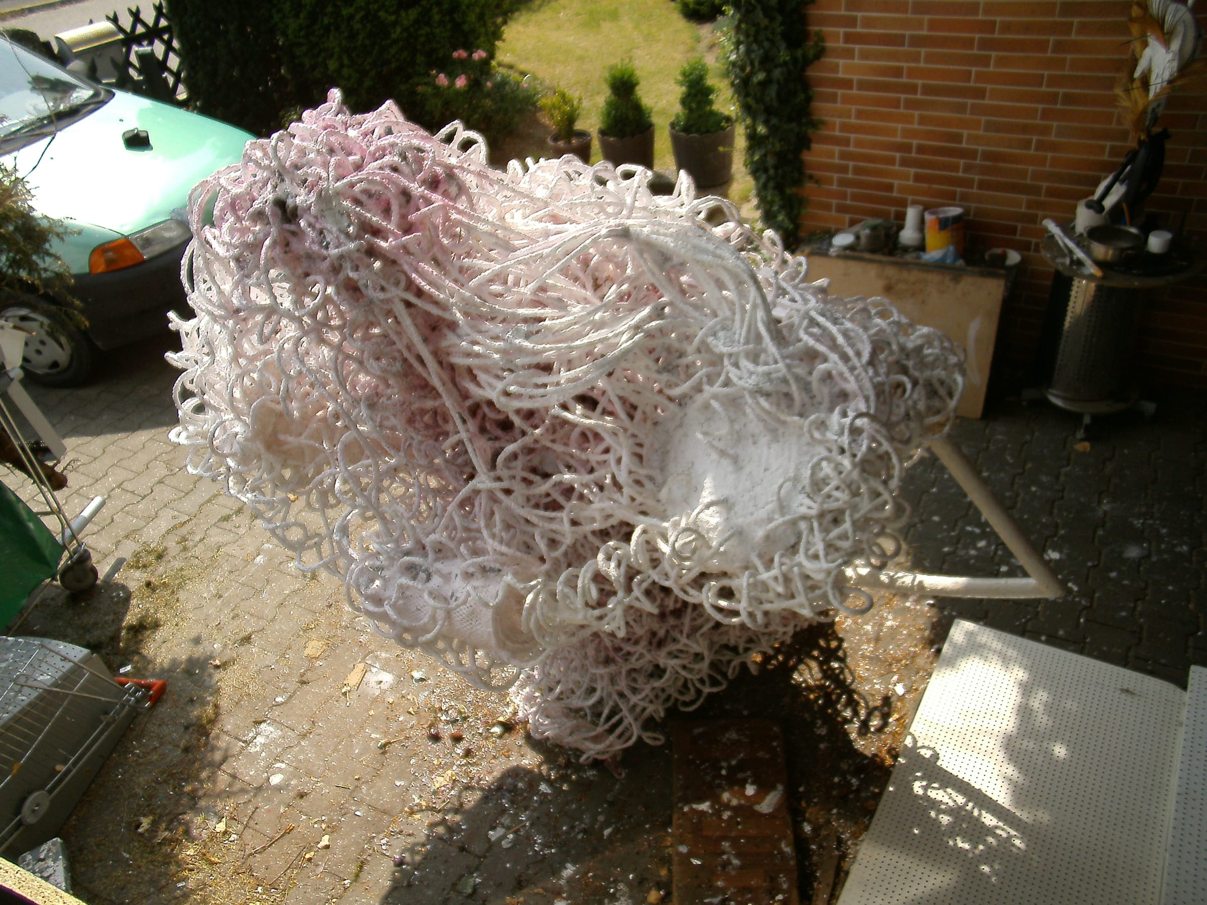 Rosa-weiße Skulptur aus Schlingen mit weissem Rohrbogen auf einem gepflasterten Hof vor einer Backsteinmauer
